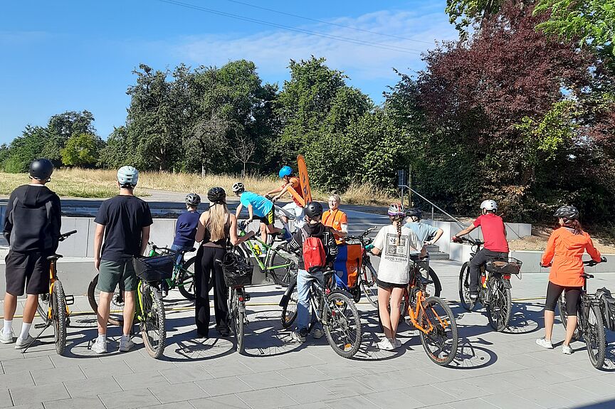 Fahrrad Projekttage am OHG eine Gruppe von Schüler*innen und Erwachsenen mit Fahrrädern steht vor einer Treppe und schaut 2 Personen zu, die Kunststücke auf Fahrrädern vorführen